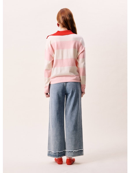 Person wearing a pink and white striped sweater with red accents, standing against a plain background.