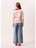Person wearing a pink and white striped sweater with red accents, standing against a plain background.