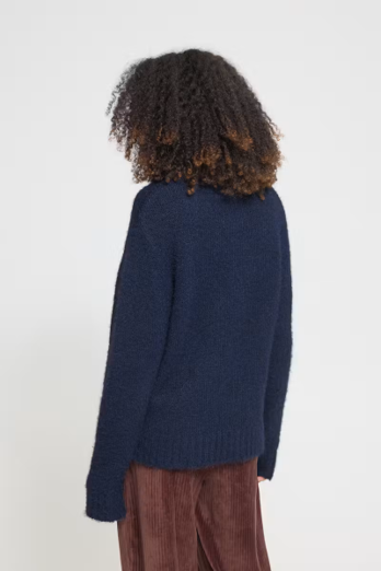 back of woman in solid navy sweater against white wall