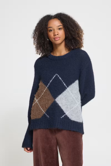 woman in navy sweater with argyle pattern in front of white wall