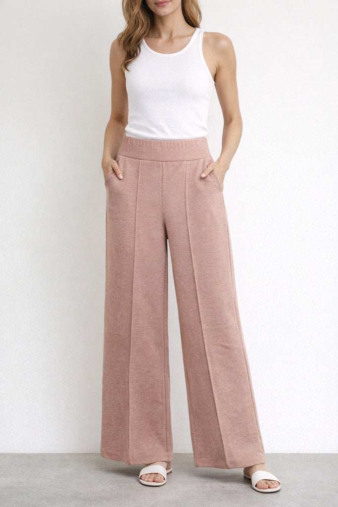 Woman wearing a white tank top and pink wide-leg pants on a plain background