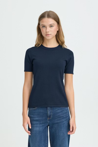 Woman wearing a navy blue t-shirt and jeans on a light gray background
