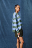 Person wearing a striped sweater and skirt against a blue backdrop