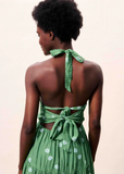 Woman wearing a green dress with open back and tied straps on a beige background