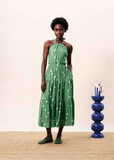Woman wearing a green dress with white polka dots standing next to a blue decorative vase on a beige surface.