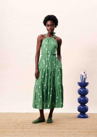 Woman wearing a green dress with white polka dots standing next to a blue decorative vase on a beige surface.