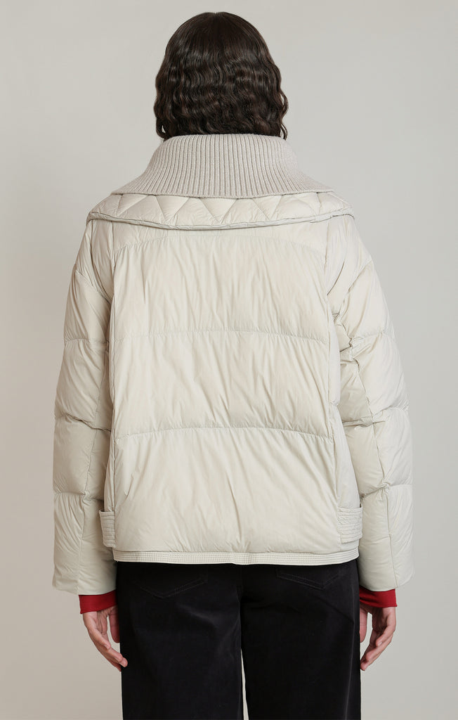 back of woman in cream puffer coat against white background