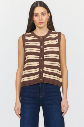 A woman modeling a sleeveless knit vest with horizontal brown, beige, and white stripes, paired with dark blue jeans against a plain white background.