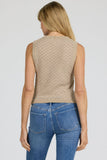 Woman wearing a beige sleeveless top and blue jeans on a plain background