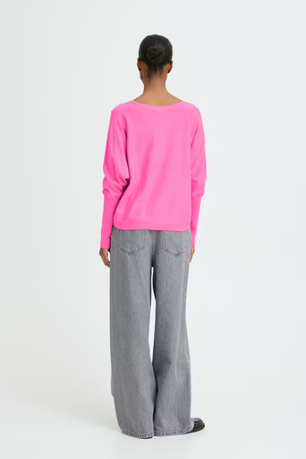 Person wearing a bright pink sweater and gray pants on a white background