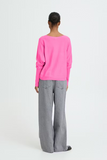 Person wearing a bright pink sweater and gray pants on a white background
