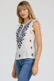 Woman wearing a white top with blue floral embroidery and blue jeans on a light gray background