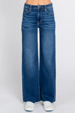 A person wearing high-waisted, wide-leg blue denim jeans with a raw frayed hem, paired with white sneakers, shown from the waist down on a light gray studio background.