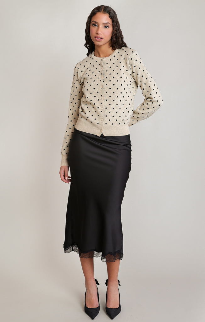 woman in polkadot sweater in black skirt against a white wall