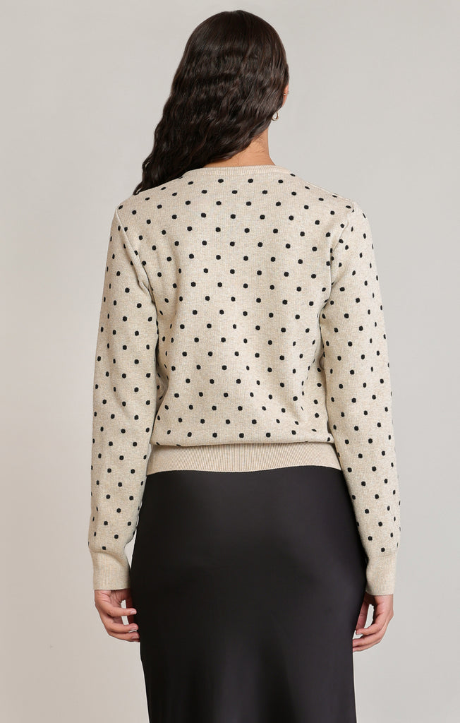 back of woman in polkadot sweater in black skirt against a white wall