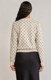 back of woman in polkadot sweater in black skirt against a white wall