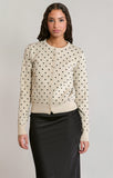 woman in polkadot sweater in black skirt against a white wall