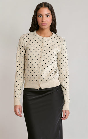 woman in polkadot sweater in black skirt against a white wall