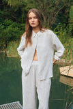 Woman in a striped outfit standing by a body of water with greenery in the background