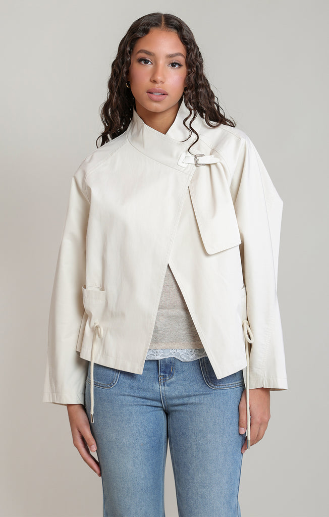 Woman wearing a cream jacket with a bow detail on a plain background