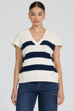 Woman wearing a white and navy striped sweater with blue jeans on a plain background