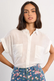 Woman wearing a white shirt with short sleeves and floral pants on a plain background