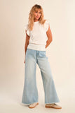 Woman wearing a white top and light blue jeans against a plain background
