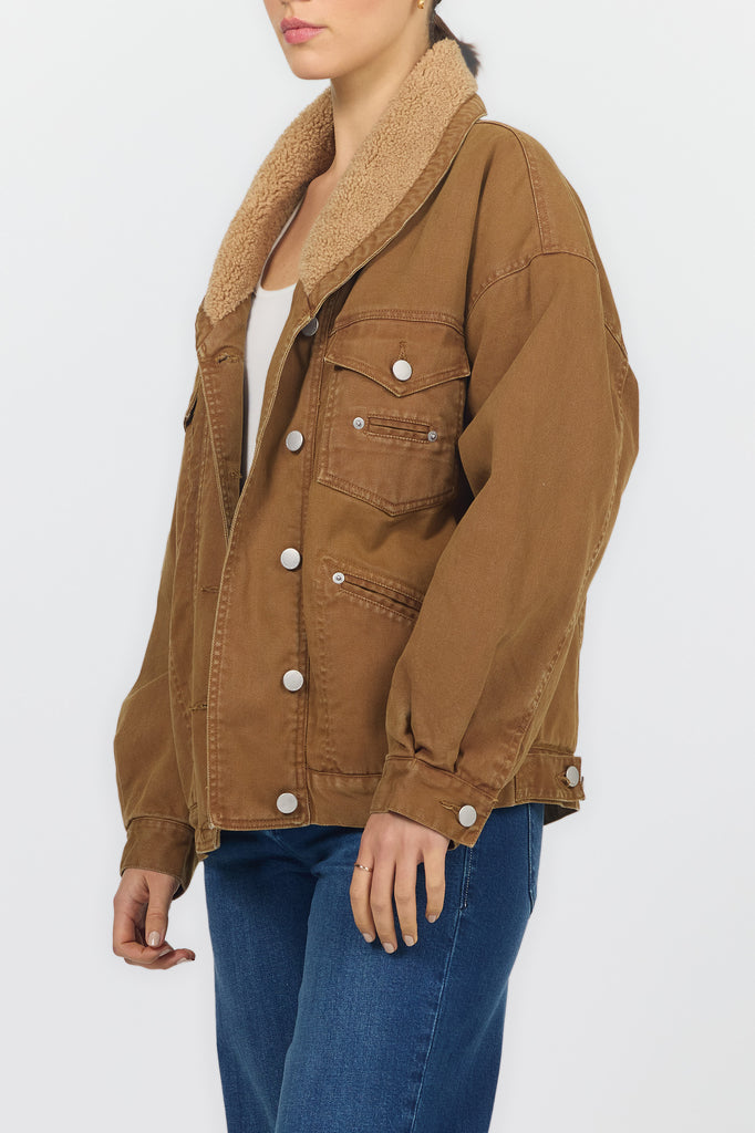 A woman wearing a brown corduroy jacket with a tan sherpa collar, paired with blue jeans, shown from the side against a light gray background.
