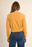 Person wearing a mustard yellow sweater and blue jeans on a beige background
