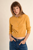 Woman wearing a mustard yellow cardigan over a crop top with blue jeans on a beige background